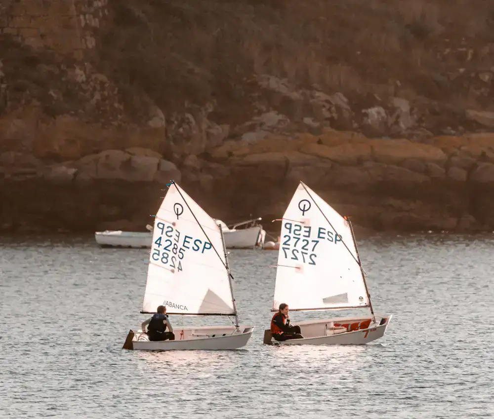 Two students sailing a small white dinghy on calm water